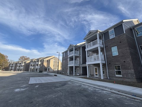 A row of new apartment buildings with a parking lot in front.