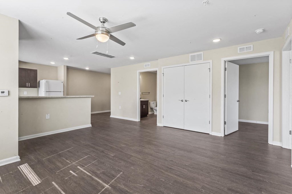 an empty living room with a ceiling fan and a kitchen