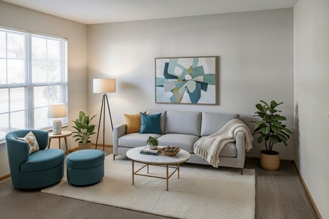 A living room with a grey couch, a blue chair, a small table, and a painting on the wall.