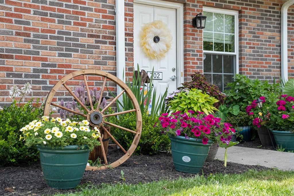 a front yard with pots of flowers and a wagon wheel