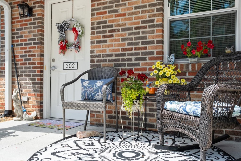 a front porch with chairs and flowers and a cat on the ground