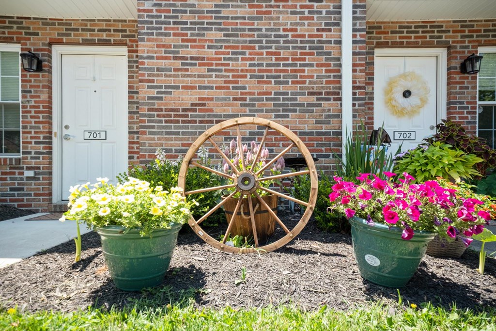 a yard with flowers and a wagon wheel in front of a building