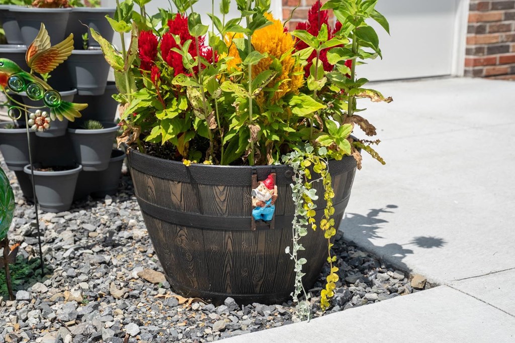 a wooden barrel filled with flowers on gravel next to a sidewalk
