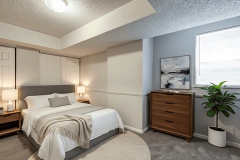 A bedroom with a bed, nightstand, and a plant.