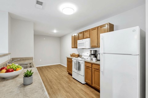 A kitchen with a white refrigerator, wooden cabinets, and a bowl of fruit on the counter.