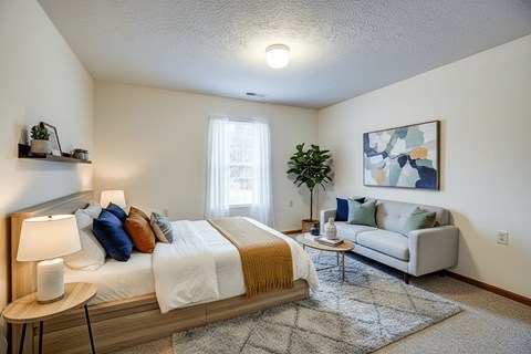 A bedroom with a bed, a couch, a table, and a painting on the wall.