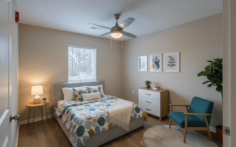 A bedroom with a bed, a chair, a nightstand, and a ceiling fan.