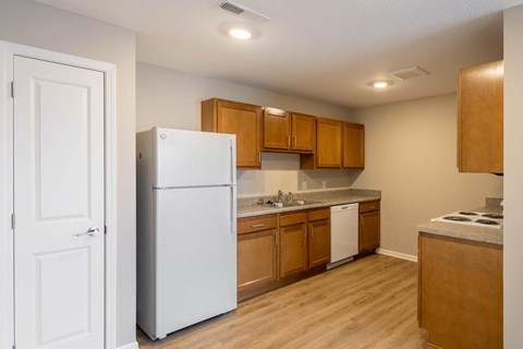 A white refrigerator stands in a kitchen with wooden cabinets and a white countertop.