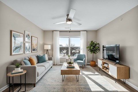 A living room with a grey couch, a coffee table, a television, and a ceiling fan.