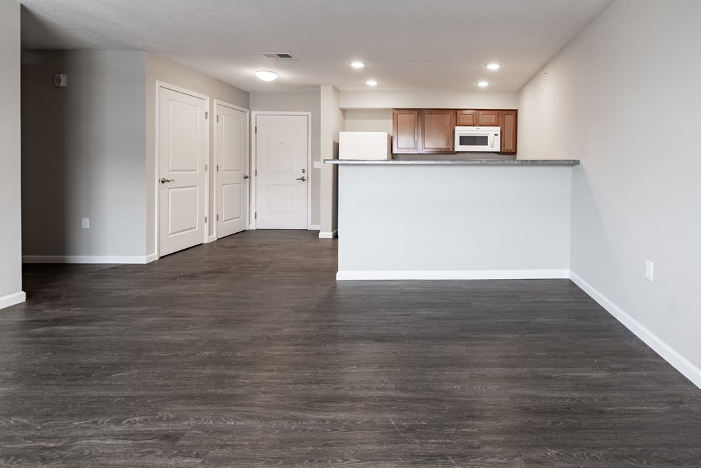an empty living room and kitchen with wood flooring and white walls