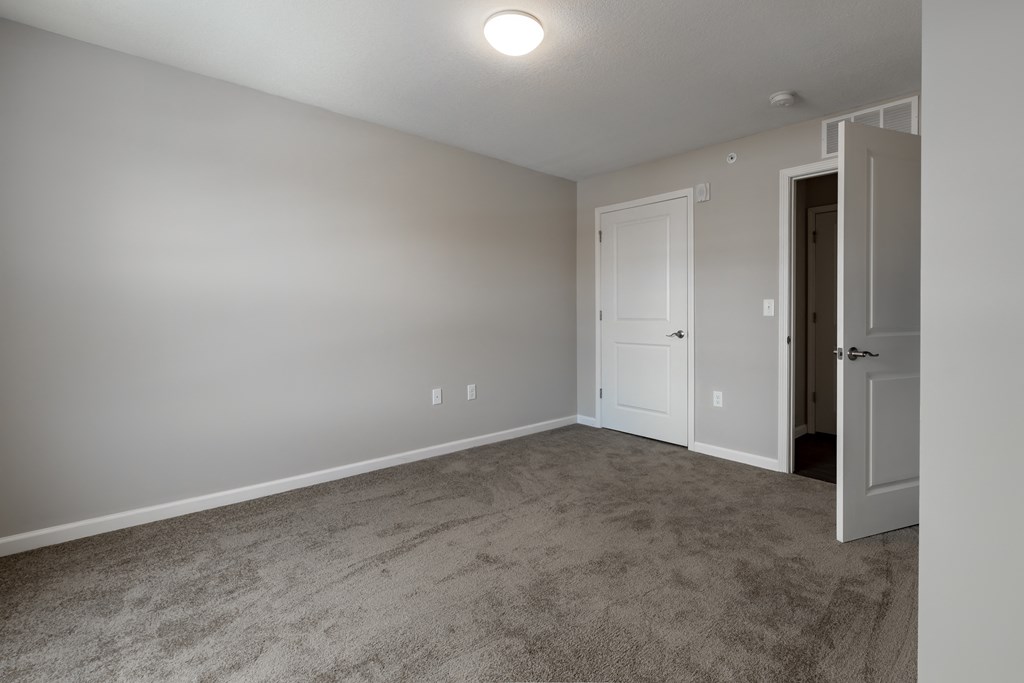 an empty living room with carpet and a door to a bedroom