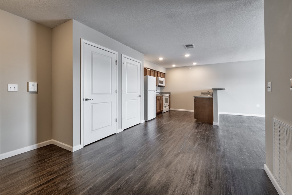 an empty living room and kitchen with white doors and wood flooring