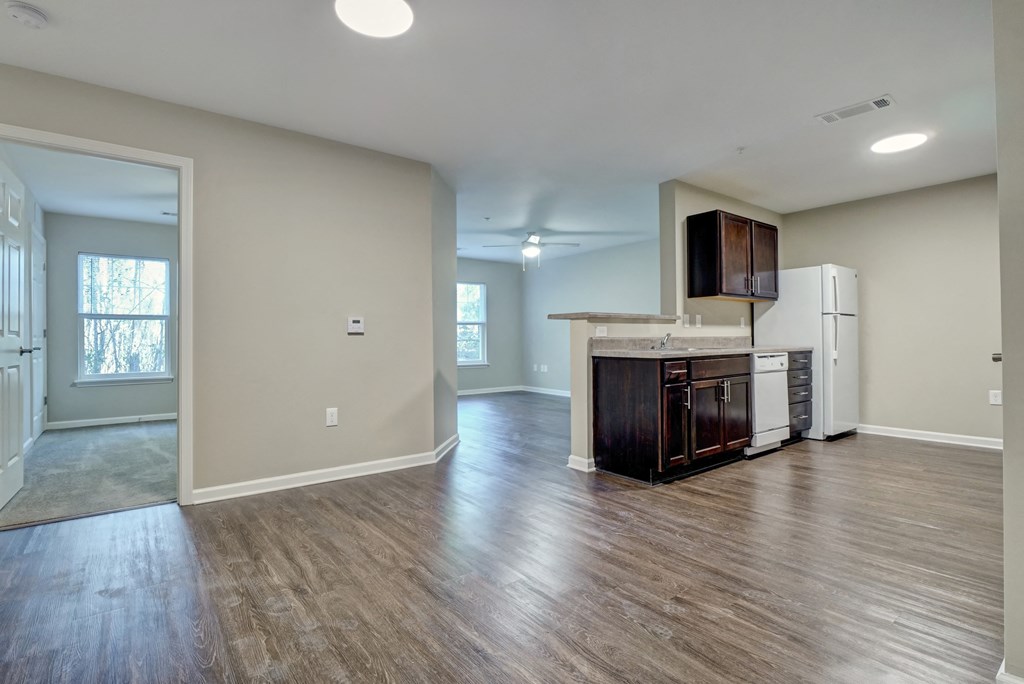 an empty living room and kitchen with a refrigerator and a microwave
