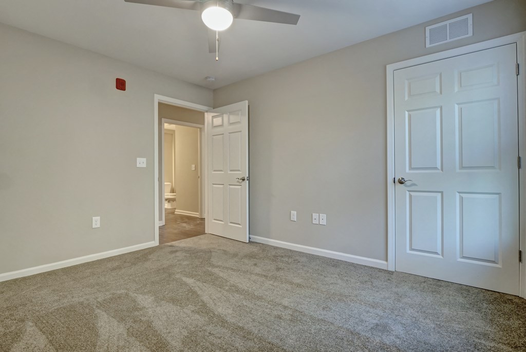 an empty living room with a ceiling fan and a door to a bathroom