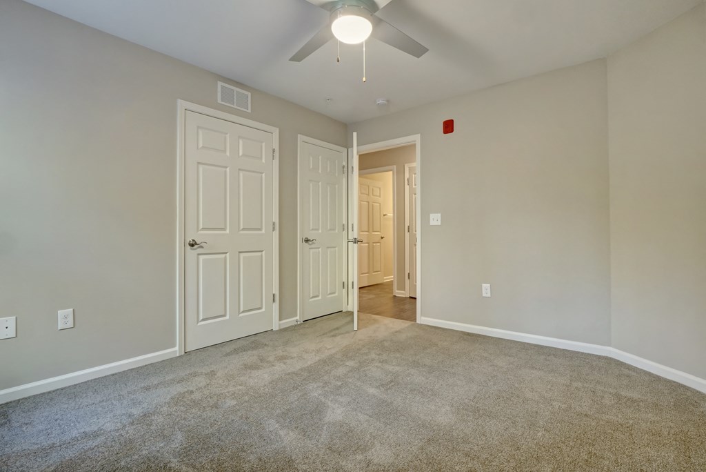 an empty living room with two doors and a ceiling fan