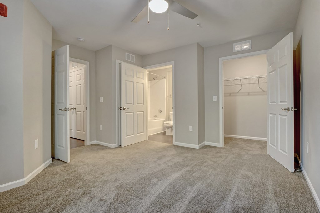 an empty bedroom with a ceiling fan and doors to the bathroom and a closet