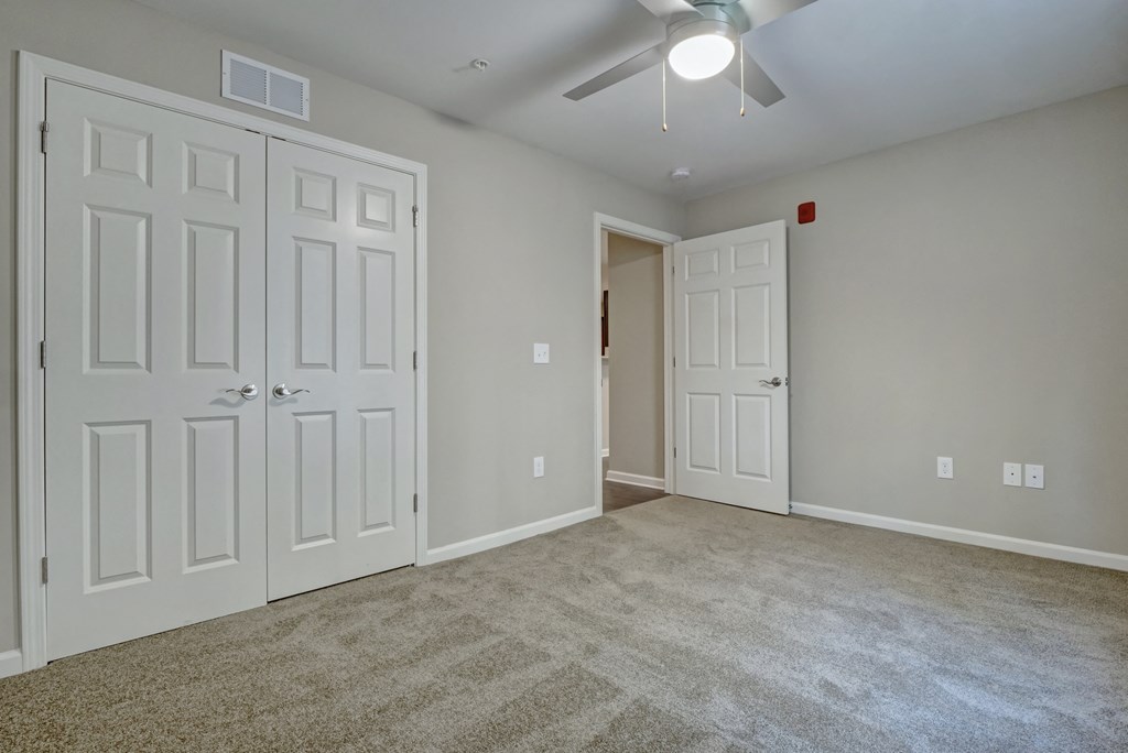 an empty living room with white doors and a ceiling fan