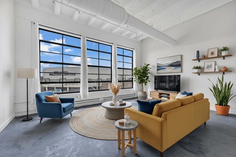 A living room with a yellow sofa, blue armchair, and a table with a vase on it.