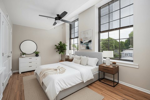 A bedroom with a large bed, a ceiling fan, and a window with a view of the outside.