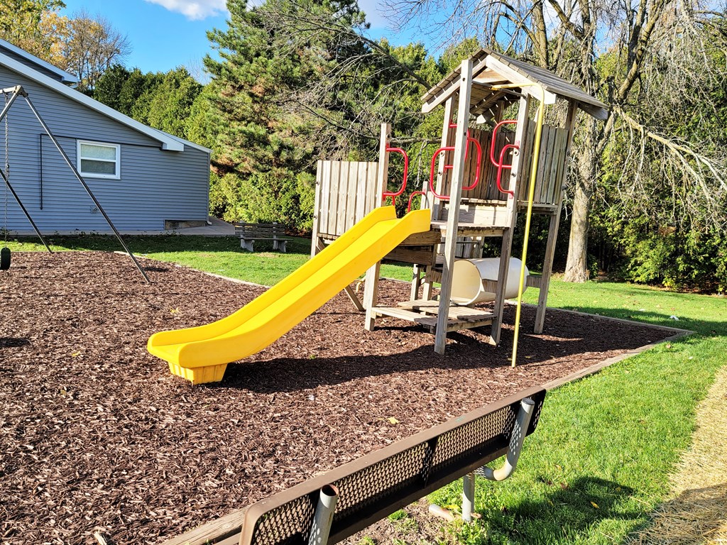 A playground with a yellow slide and a wooden structure.