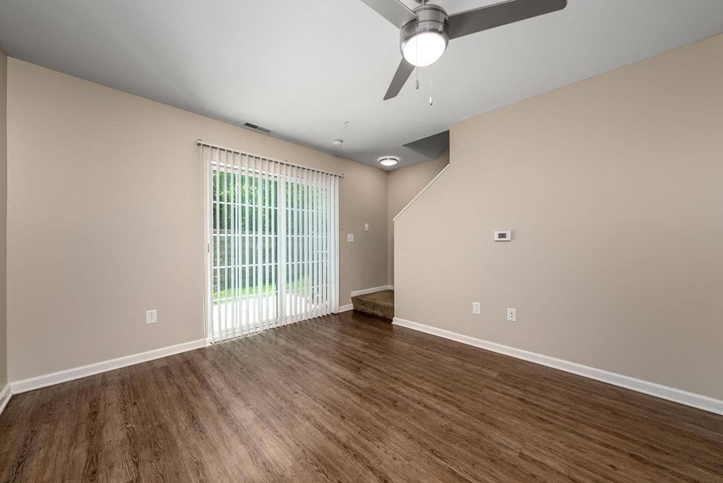 an empty living room with a large window and a ceiling fan