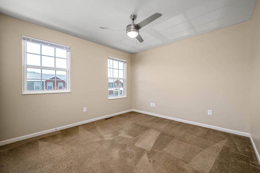 an empty room with a ceiling fan and two windows