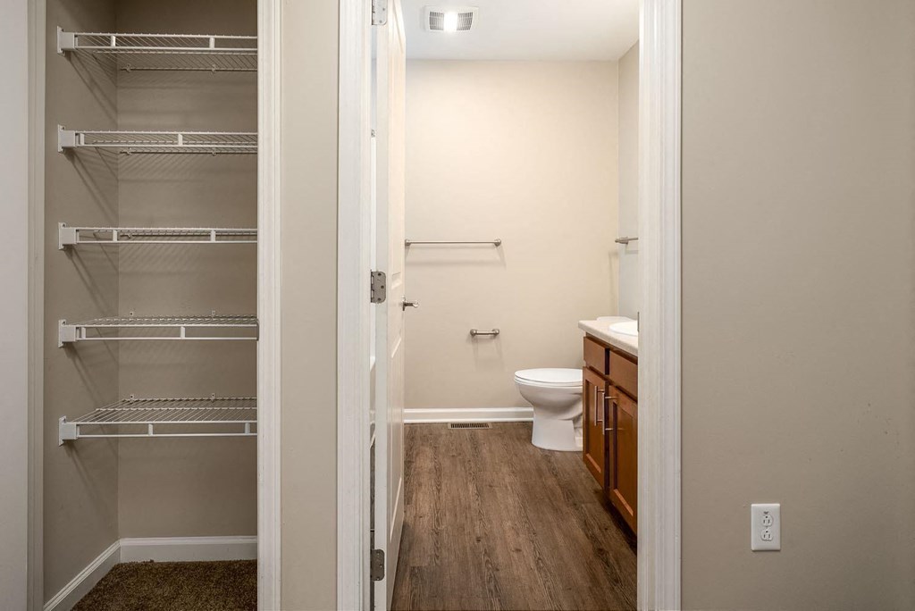 A white toilet is in a small bathroom with a walk-in closet.