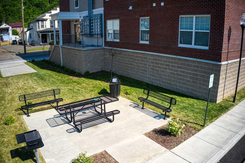 a patio with three benches and a trash can in front of a brick building