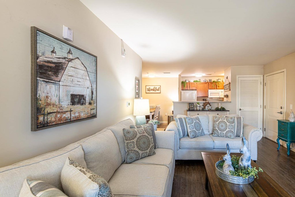 A living room with a grey couch and a painting of a barn on the wall.