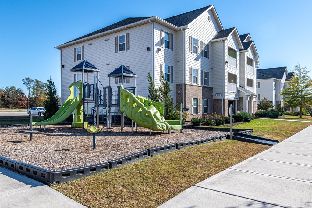 A playground with a green slide in front of a white apartment building.