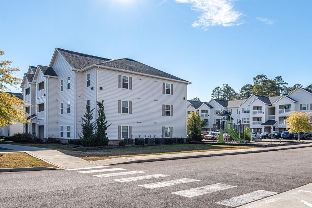 A white building with a grey roof is in the background of a street with a crosswalk.