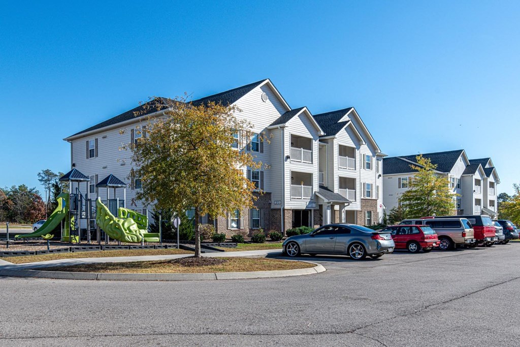 Apartment complex with a playground and cars parked in front.