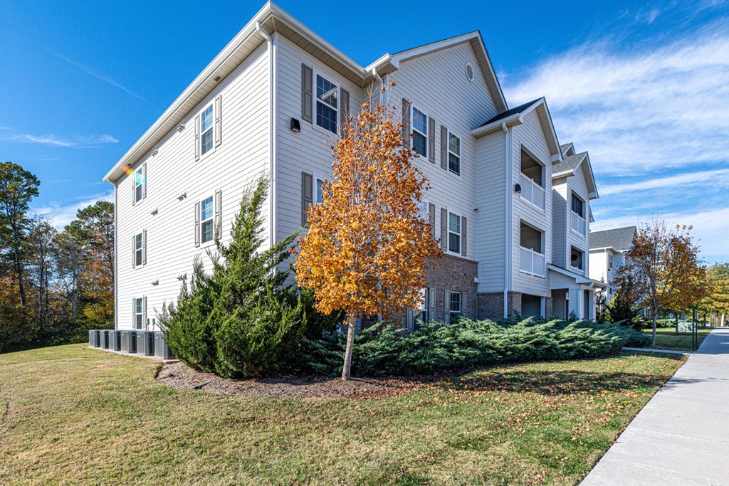 A white two-story apartment building with a yellow tree in front.