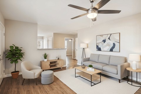A living room with a grey couch, a white rug, and a ceiling fan.