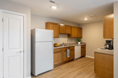 A white refrigerator stands in a kitchen with wooden cabinets and a counter.