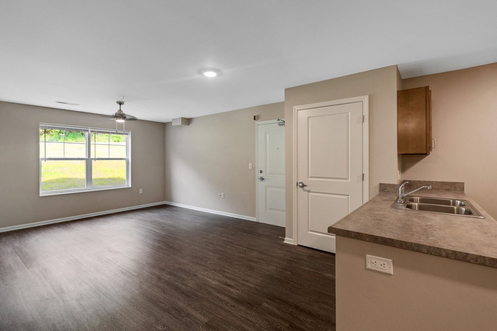 an empty living room with a kitchen and a window