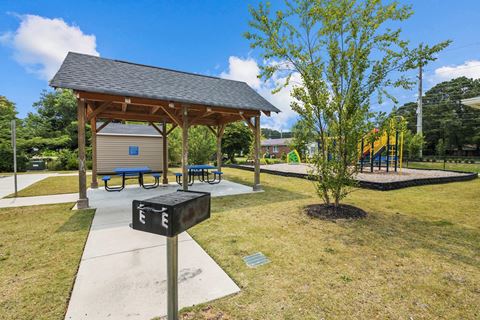 a picnic pavilion with benches and a playground in a park