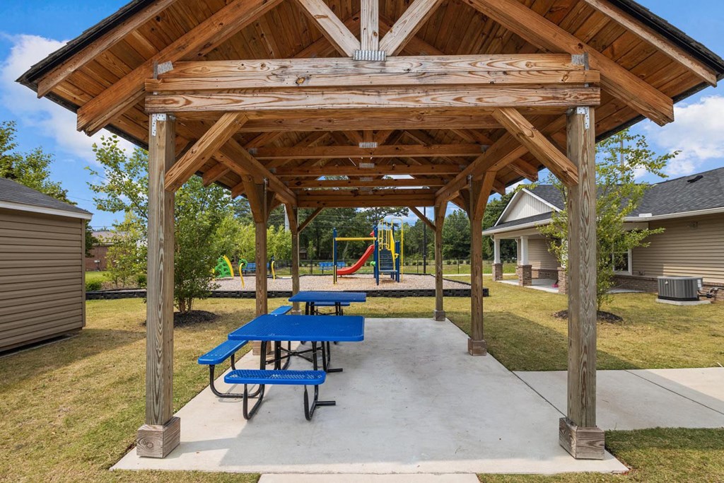 a picnic pavilion with benches and a playground in the background