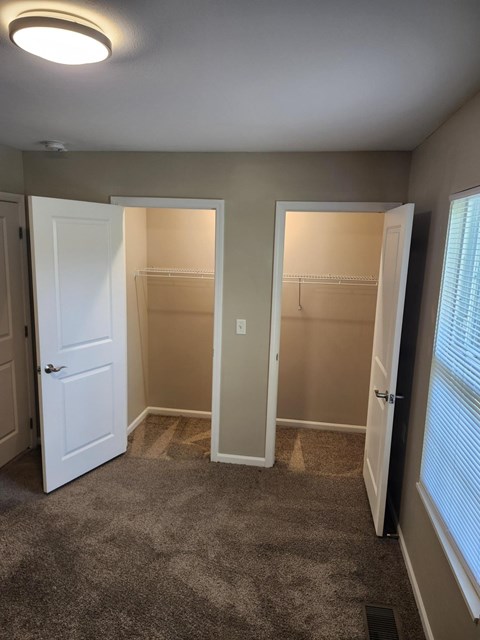 A room with two open closets and a carpeted floor.