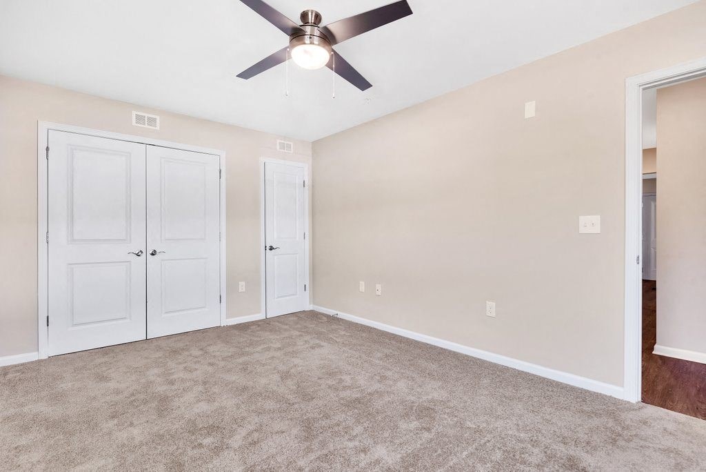 an empty living room with a ceiling fan and a closet