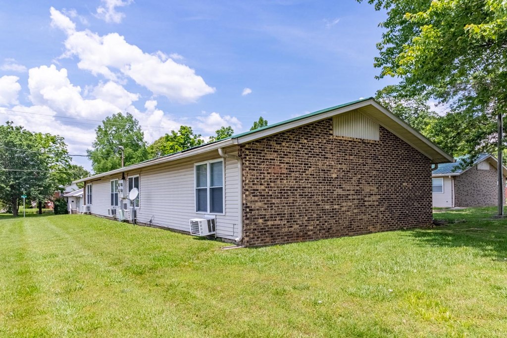 a small white house with a brick wall and a grassy yard in front of it