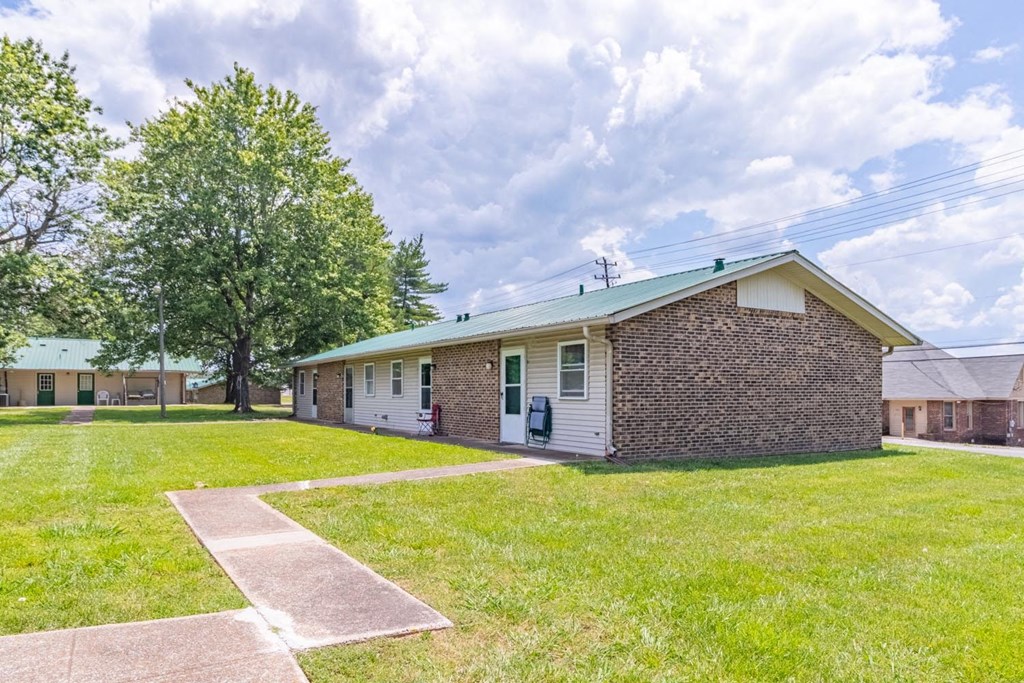 a brick building with green shutters and a tree in the background