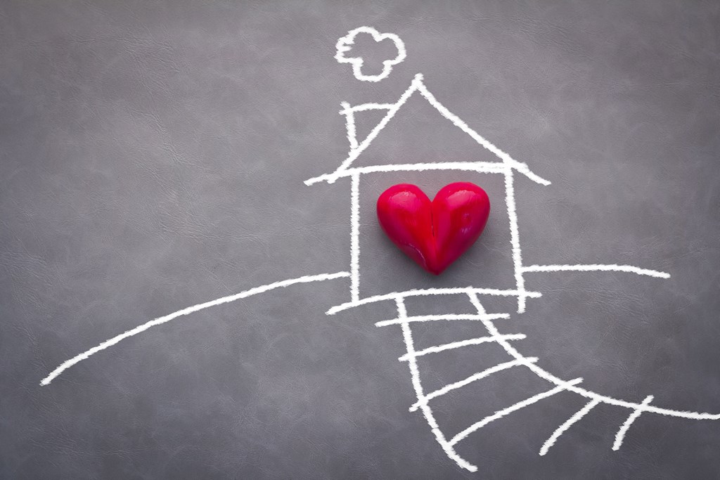 A red heart sits on a drawing of a house on a chalkboard.