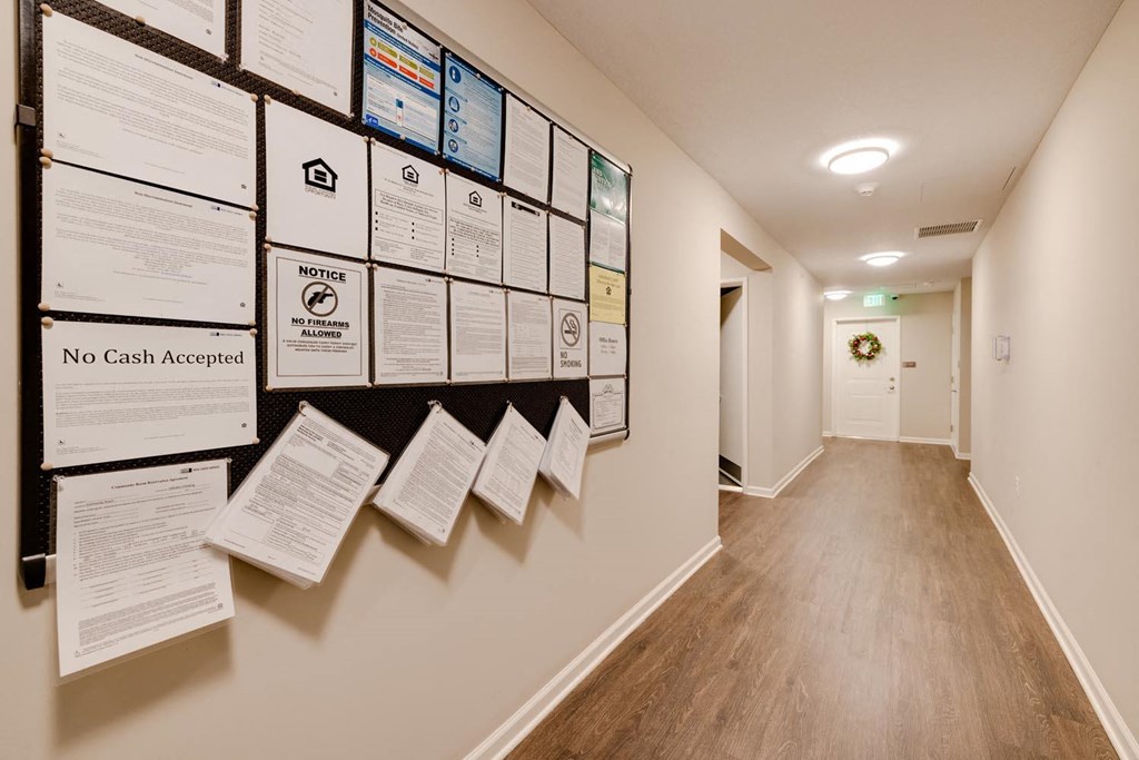 a bulletin board on the wall of a hallway with a door in the background