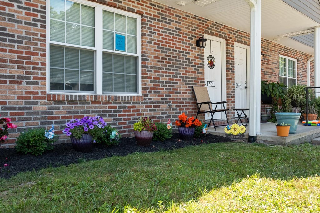 the front porch of a brick house with flowers and a chair