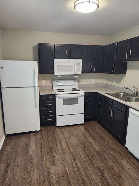 A kitchen with a white fridge, black cabinets, and a white stove.