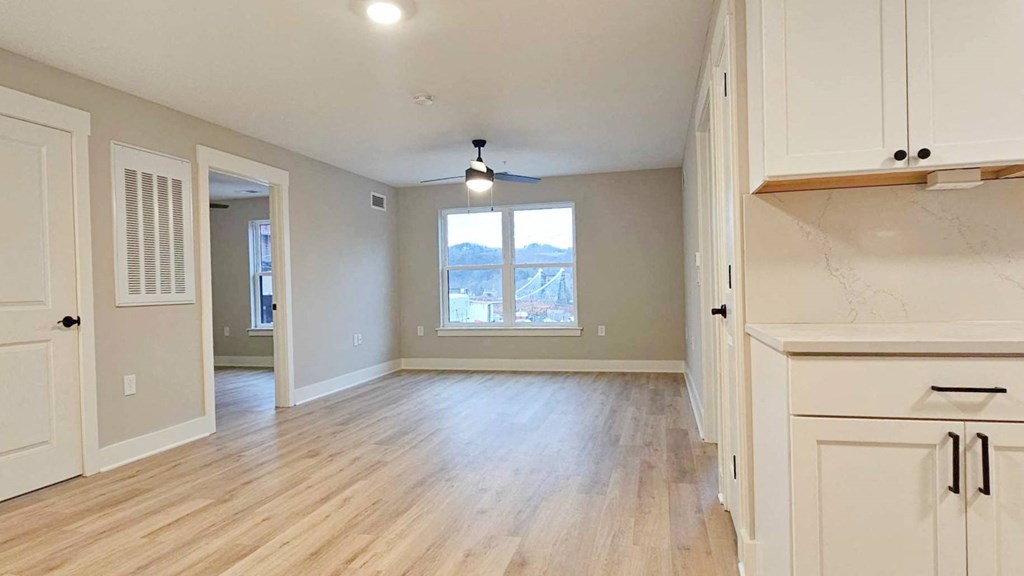 an empty living room and kitchen with a large window and wooden floors