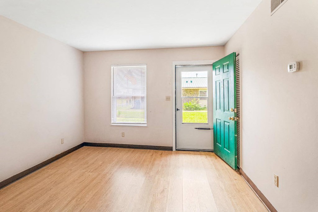 an empty room with a green door and two windows