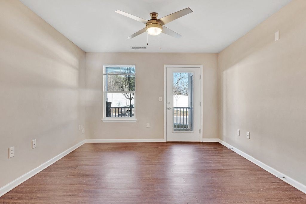 an empty living room with a ceiling fan and a door to a balcony