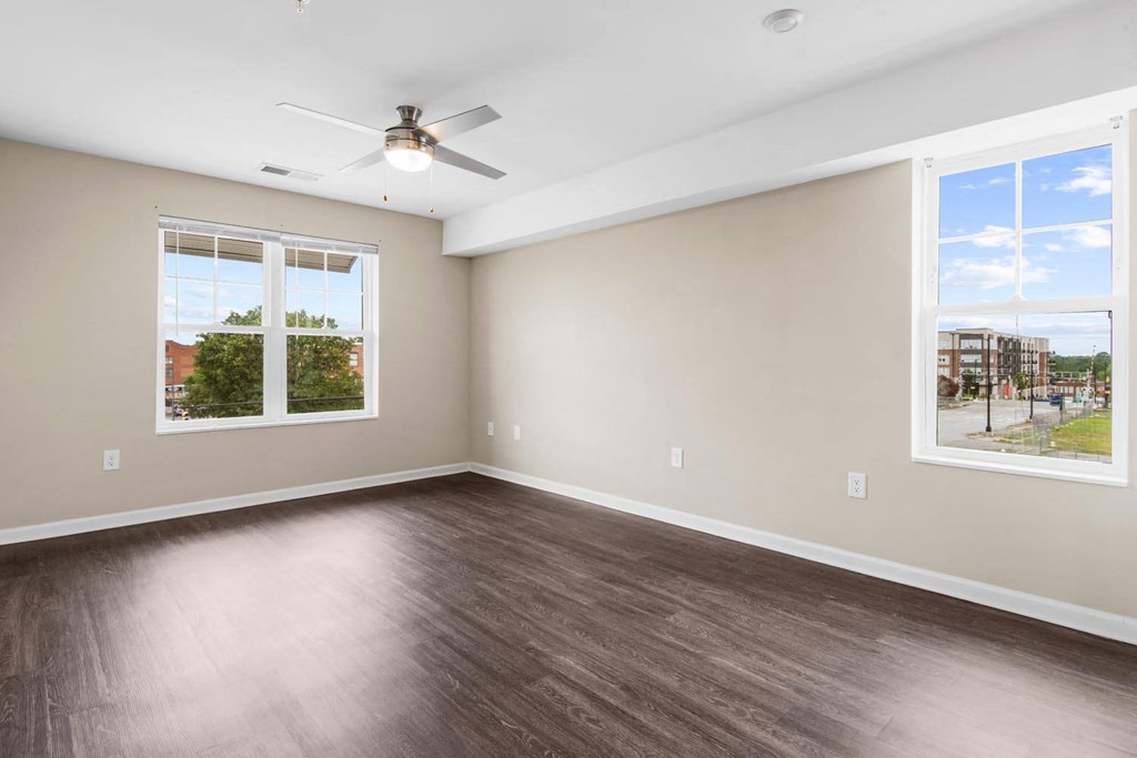 an empty bedroom with two windows and a ceiling fan